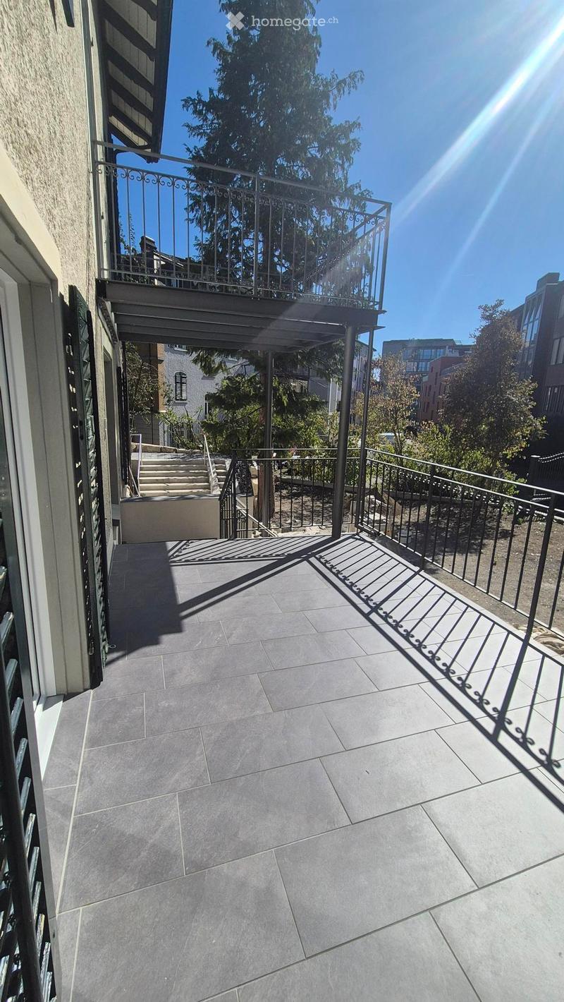 Balcony with grey tiled floor, metal railing, and steps leading to a lower level.