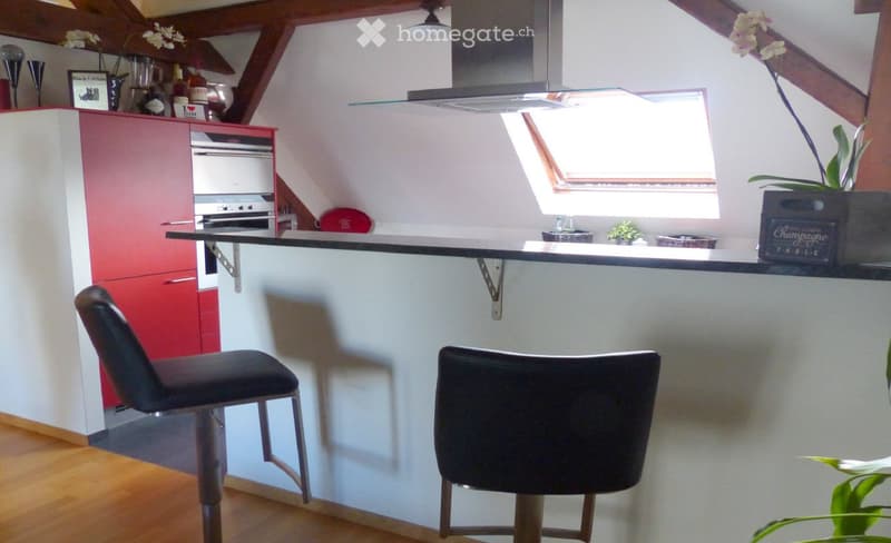 Modern kitchen with red and white cabinets, a central island with bar stools, an oven, and various kitchen items on the counter, including a blender, wine bottles, and decorative items.