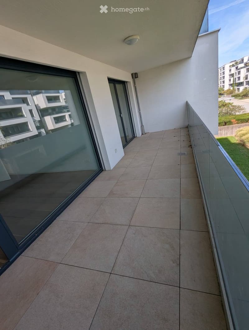 Modern balcony with tiled floor, glass railing, and large sliding glass door leading to the interior.