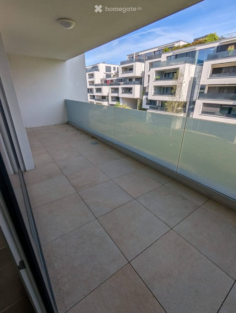Modern balcony with tiled floor, glass railing, and view of contemporary apartment buildings.
