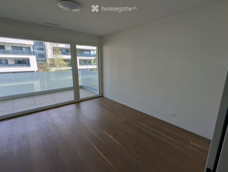 Empty room with wooden flooring, white walls, and large sliding glass doors leading to a balcony.