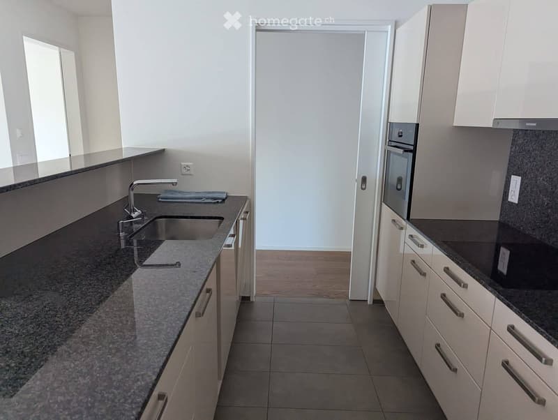 Modern kitchen with white cabinets, granite countertops, stainless steel sink, and built-in oven.