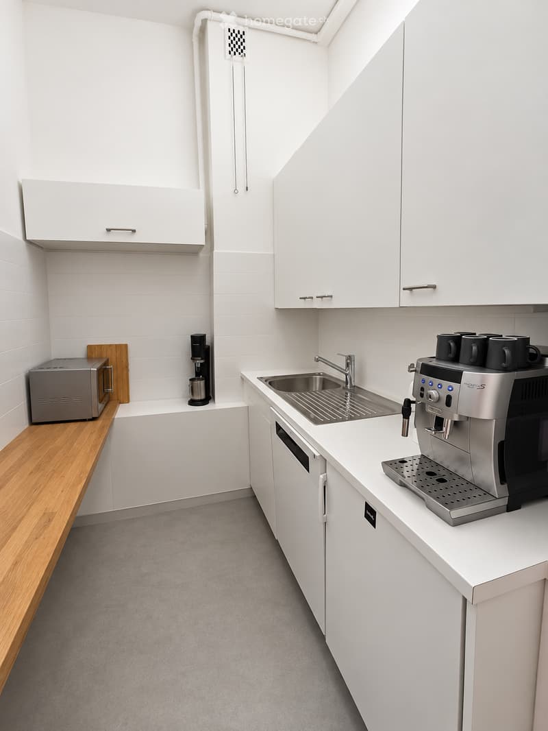 Modern, compact kitchen with white cabinets, stainless steel appliances, and a wooden countertop.