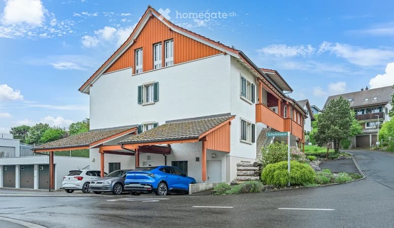Two-story residential building with white walls, orange wooden trim, and a garage. Three cars are parked in front of the building.