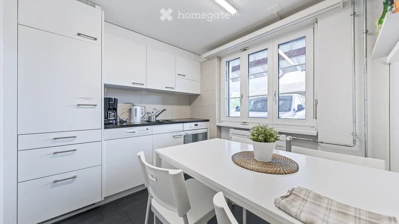 Modern kitchen with white cabinets, a sink, coffee maker, and a small dining area with a table and chairs.