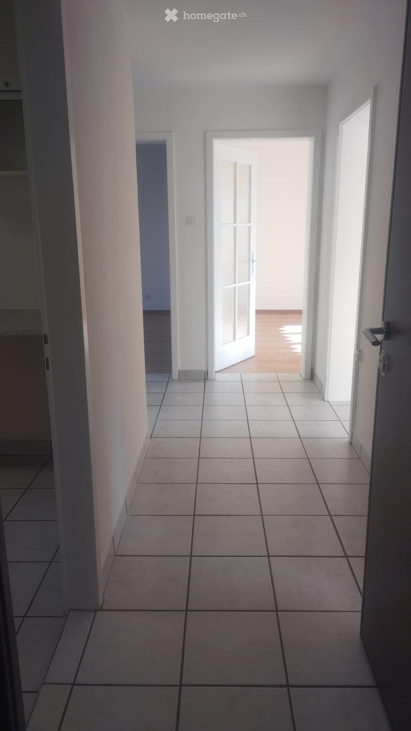 White tiled floor, white walls, open doors, wooden floor in distance