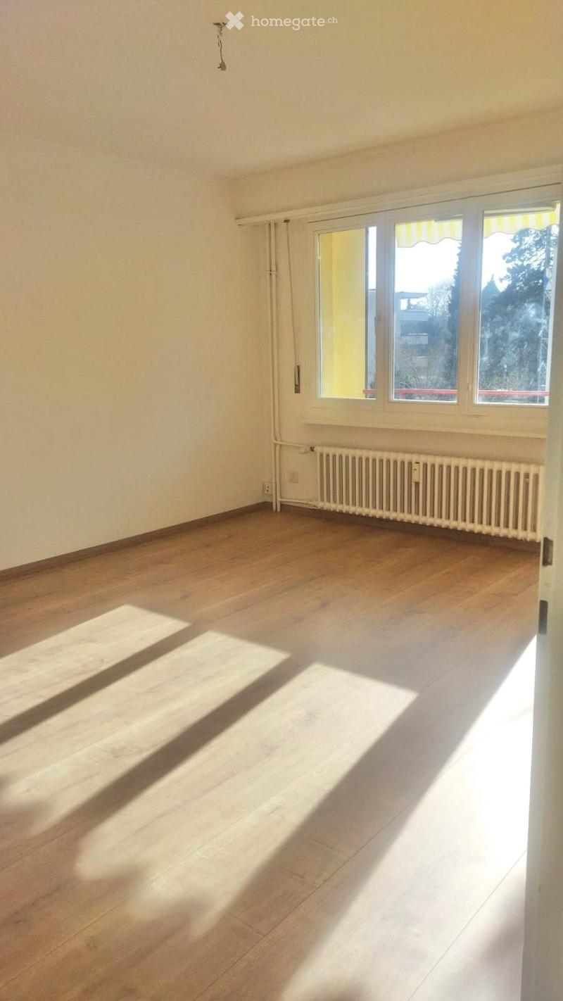 Empty room with hardwood floors, white walls, a large window with balcony, and trees visible outside