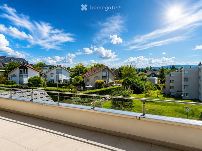 Balcony with a modern glass railing overlooking a well-maintained garden and residential area with houses and trees.