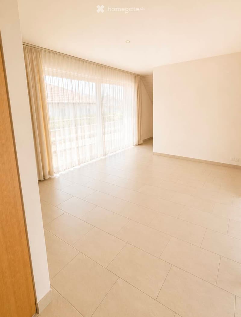 Empty room with light-colored tiled flooring, white walls, large window with sheer curtains, and recessed ceiling lighting.