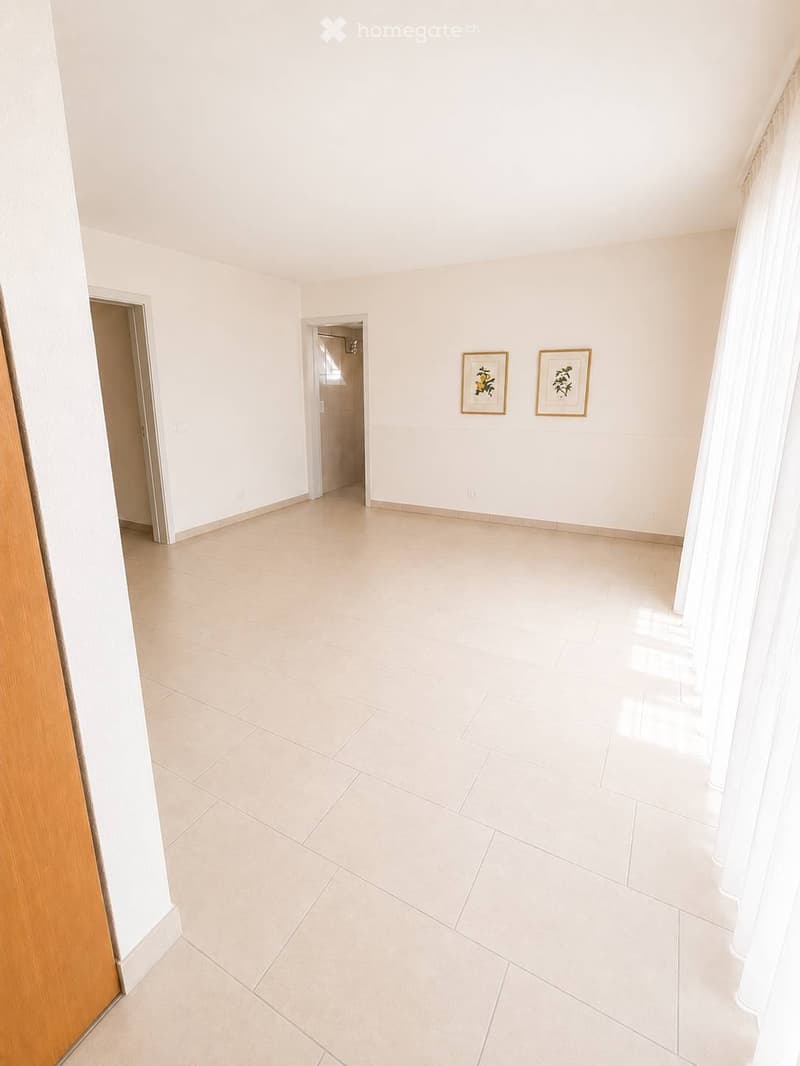 Empty room with white walls, tiled floor, and two framed pictures on the wall. Two doorways lead to other spaces.