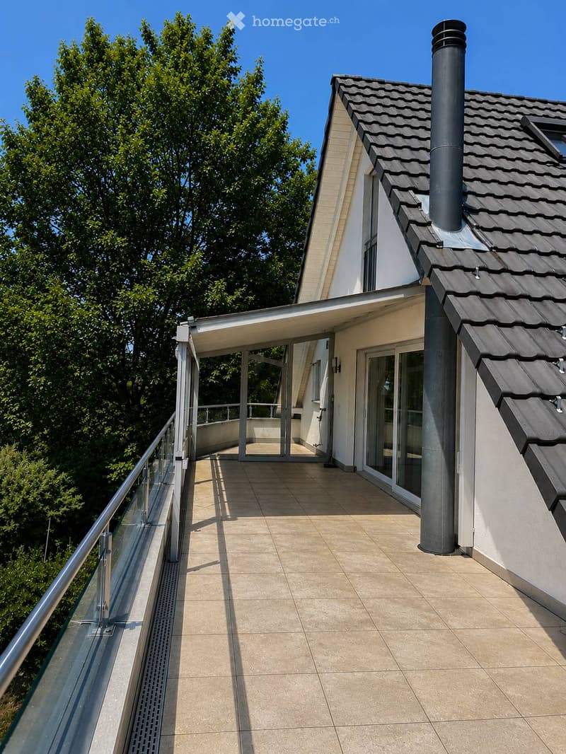 Balcony with tiled floor, glass railing, and access to the house through large glass doors.