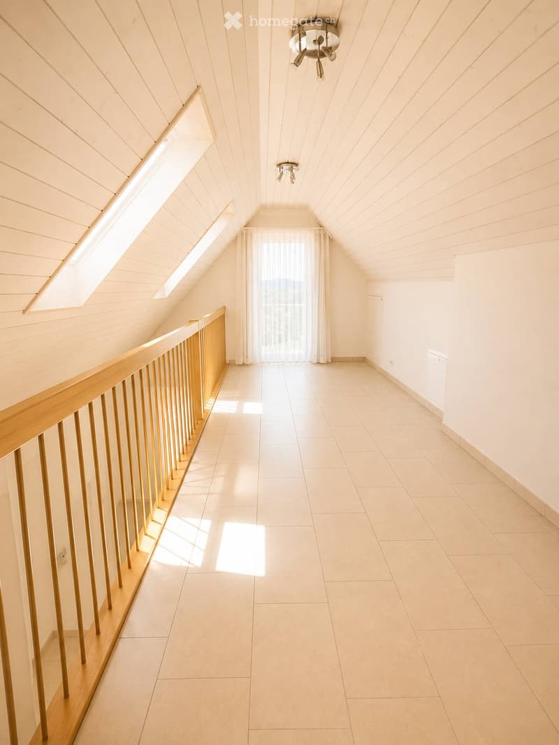 Bright, empty hallway with wooden railing, tiled floor, and skylight windows allowing natural light to enter.