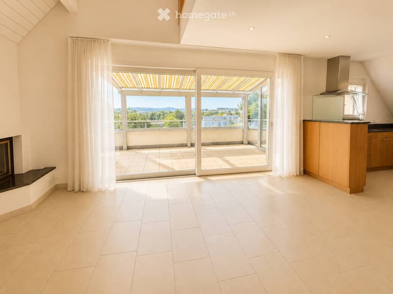 Bright, open room with white tiled flooring, a fireplace, a kitchen area with cabinets and a range hood, and large sliding glass doors leading to a balcony with a scenic view.