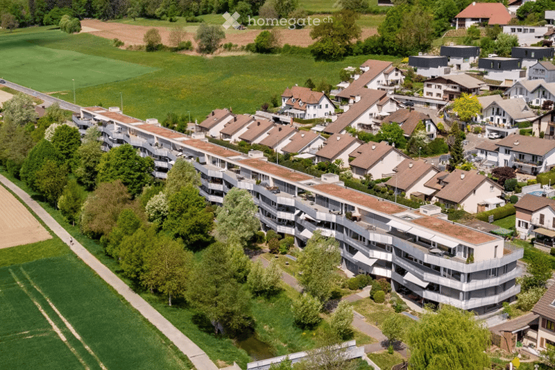 Aerial view of a residential area with multiple apartment buildings and houses, surrounded by green fields and trees.