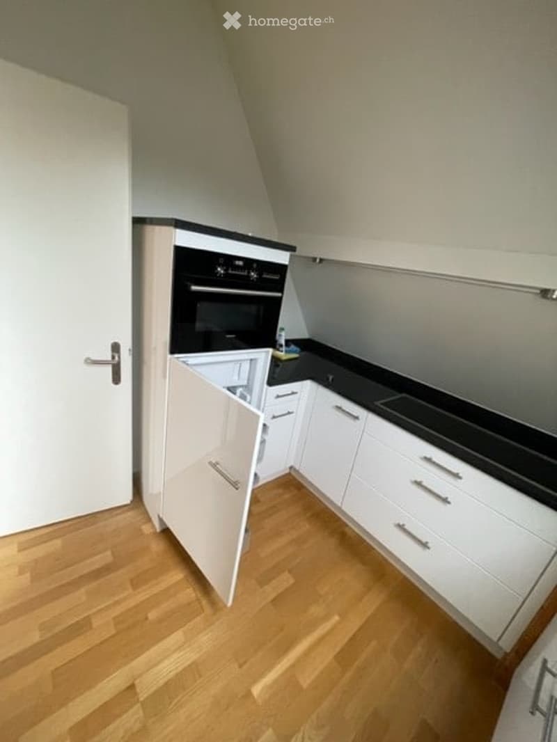 Modern kitchen with white cabinets, black countertop, and an open oven door revealing interior compartments.