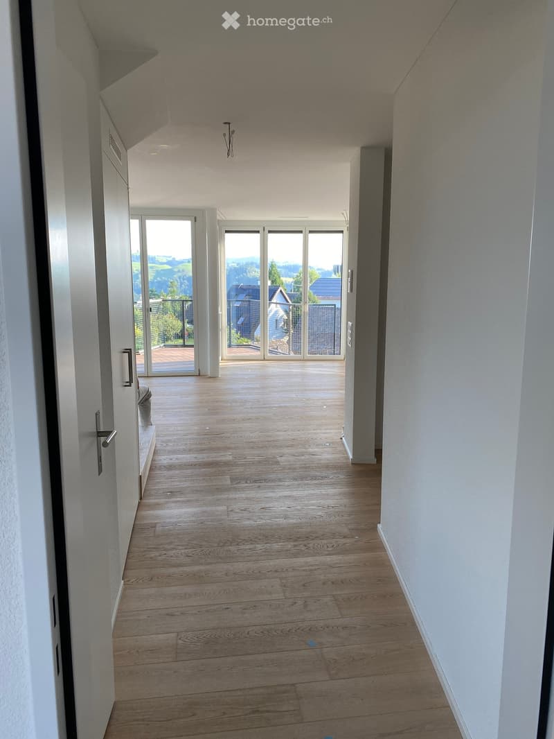 Bright hallway with wooden flooring, white walls, and large glass doors leading to a balcony or outdoor area.