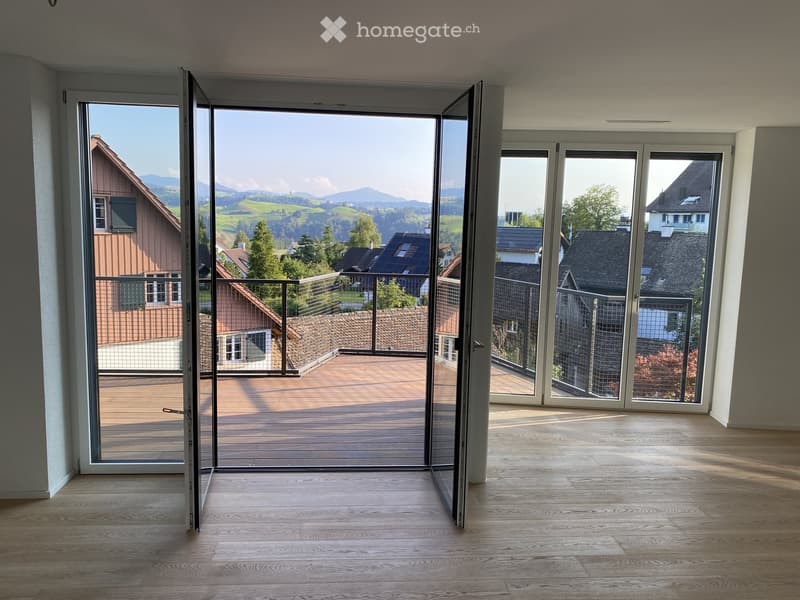 Empty room with wooden flooring and large sliding glass doors leading to a balcony with a scenic mountain view.