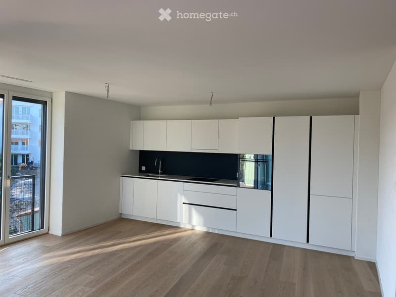 Modern kitchen with white cabinets, a dark countertop, and a wooden floor. Features a sink with a faucet and a large window with a view of the balcony.