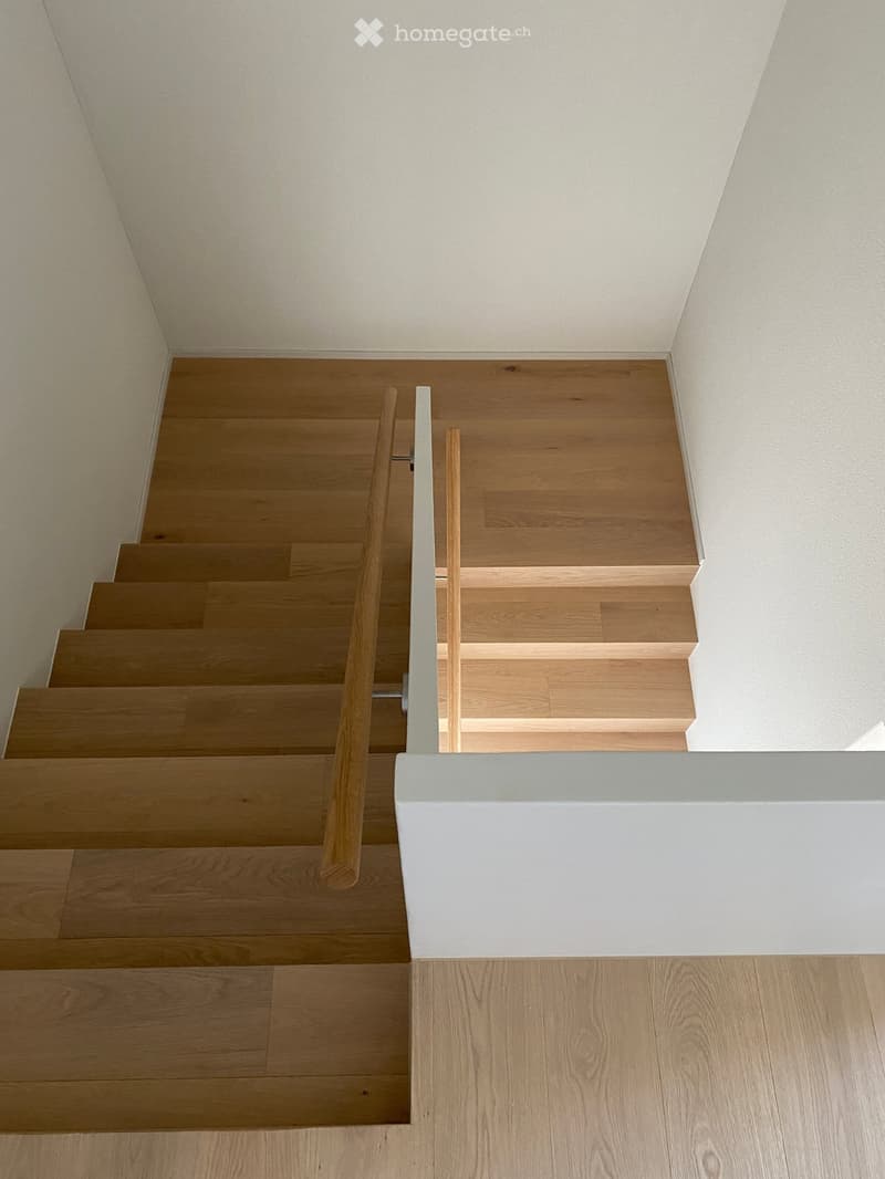 Wooden staircase with a modern, minimalist design, featuring light-colored wooden steps and a sleek white wall railing.