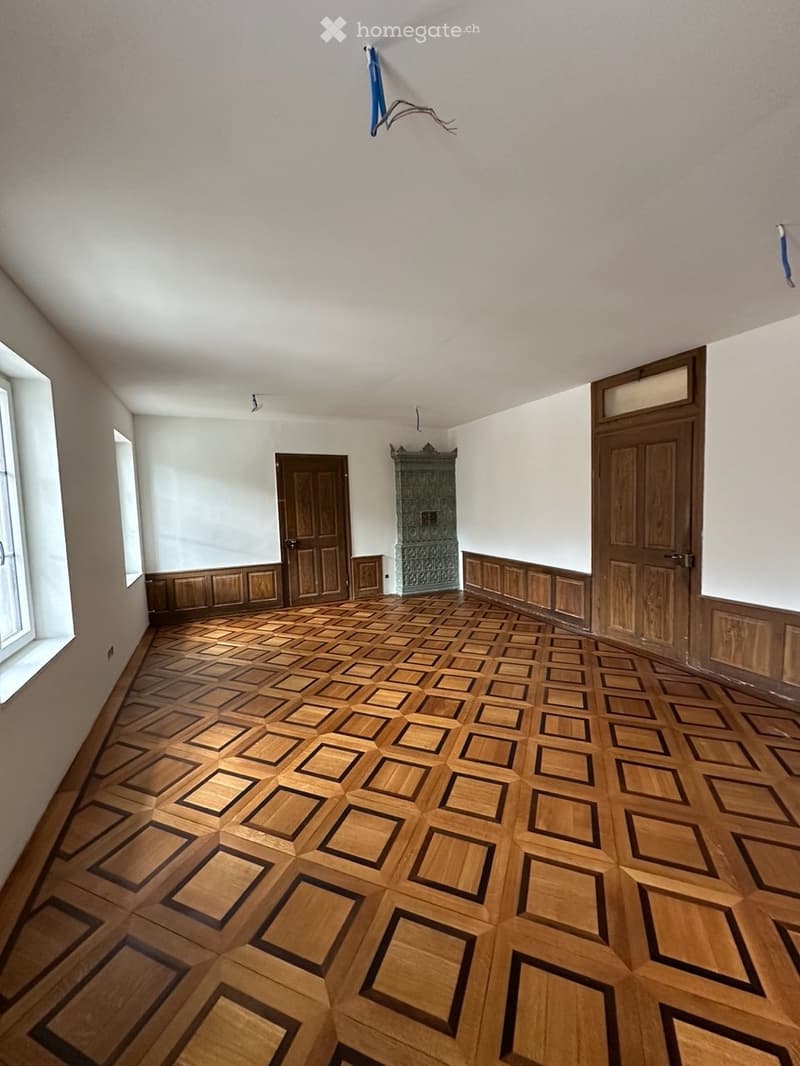 Empty room with wooden parquet flooring, white walls, and wooden doors. No furniture or equipment present.