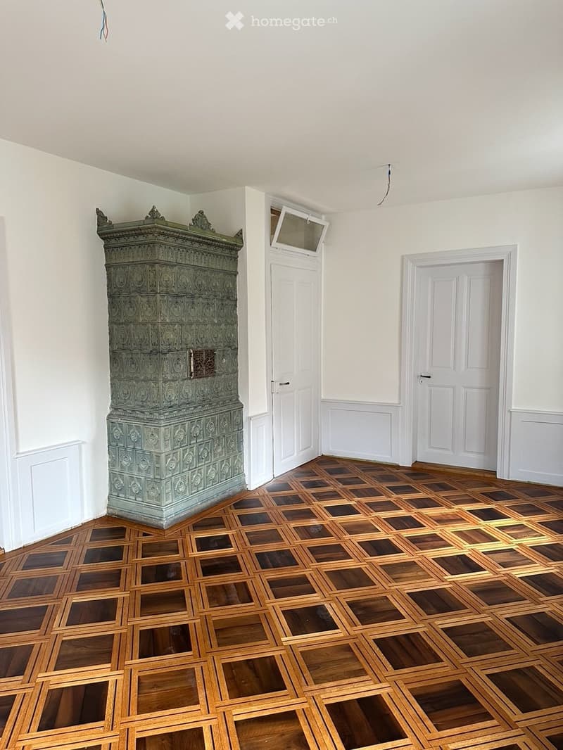 Empty room with white walls, wooden floor, and a large decorative metal cabinet. Two doors are visible, one with a small window above it.