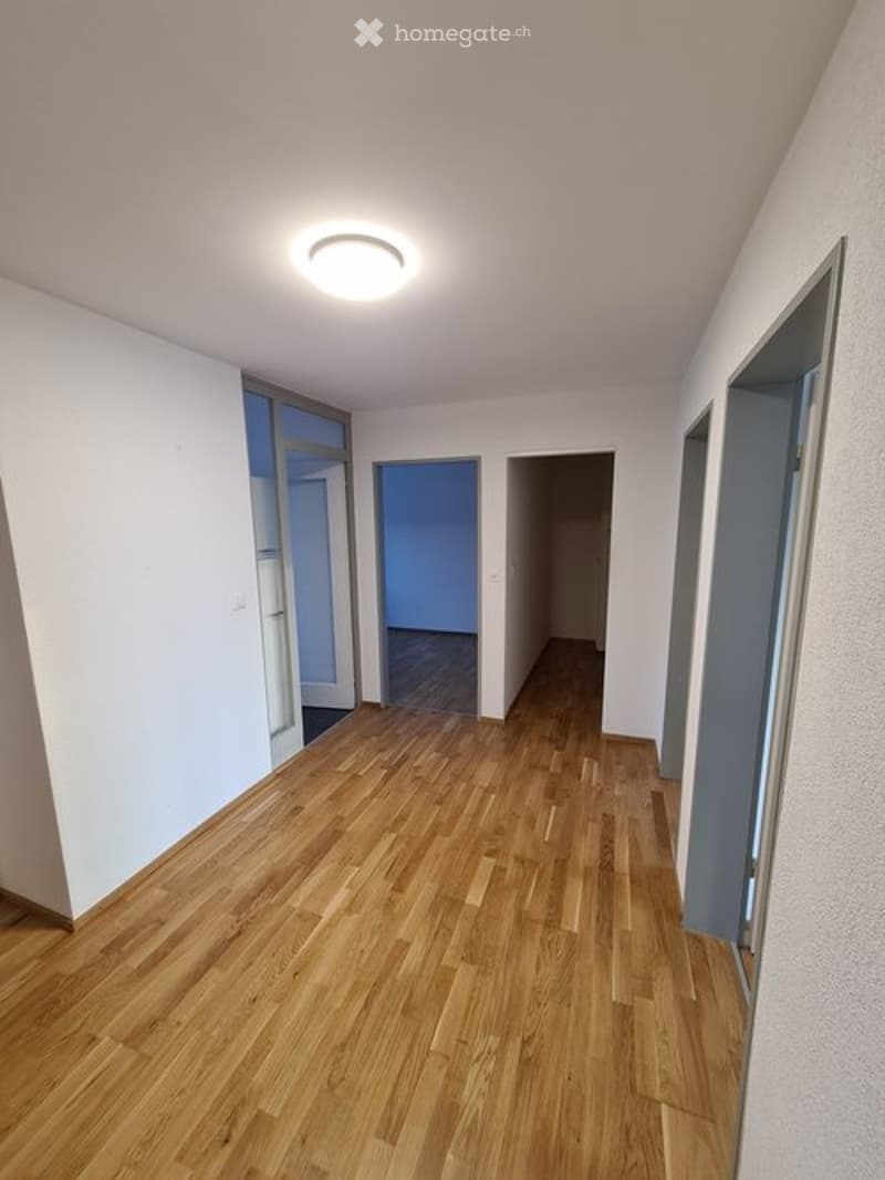 Empty hallway with wooden flooring, white walls, and recessed lighting. Doors lead to adjacent rooms.