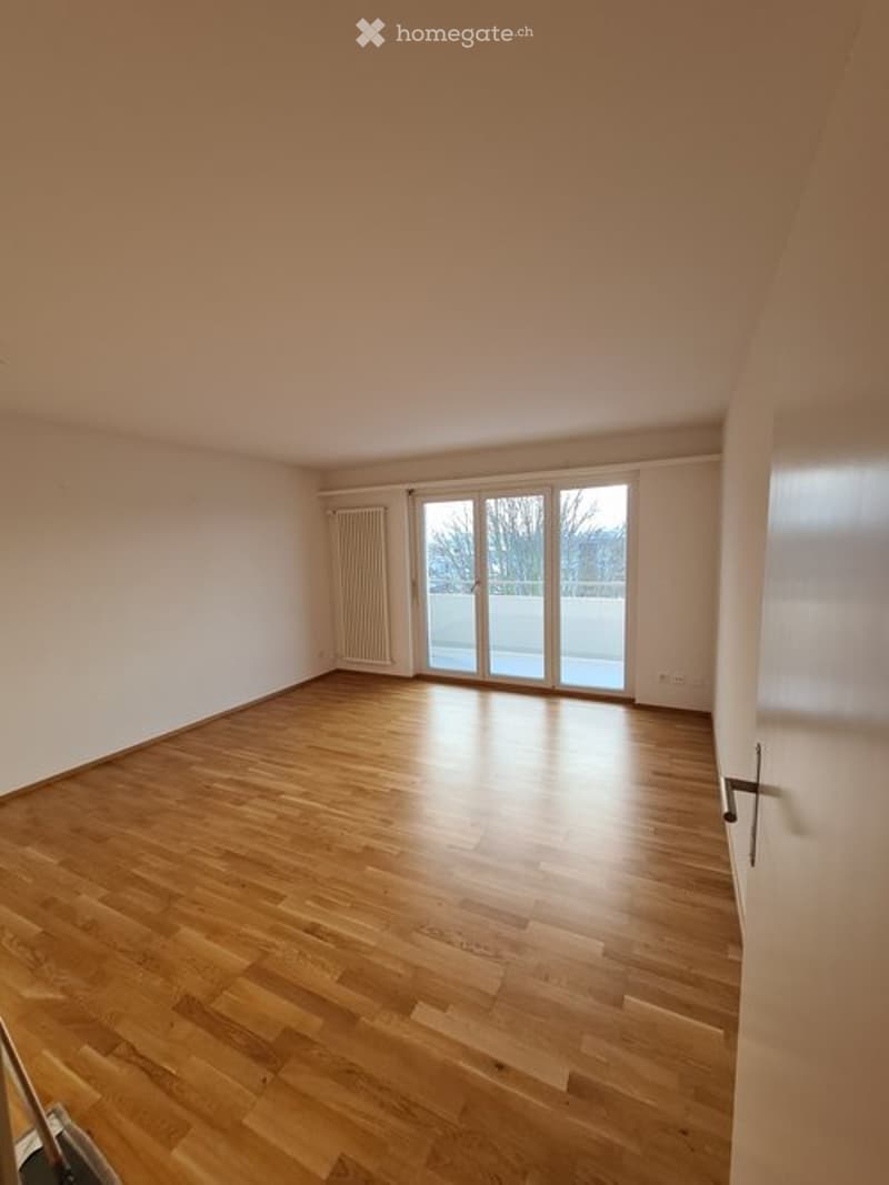 Empty room with wooden flooring, white walls, and large sliding glass doors leading to a balcony.