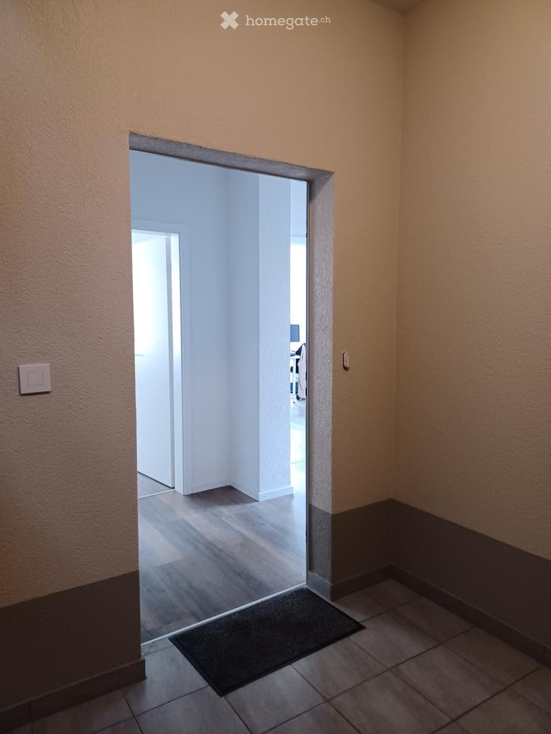 Empty hallway with tiled floor, beige walls, and a glass door leading to another room.
