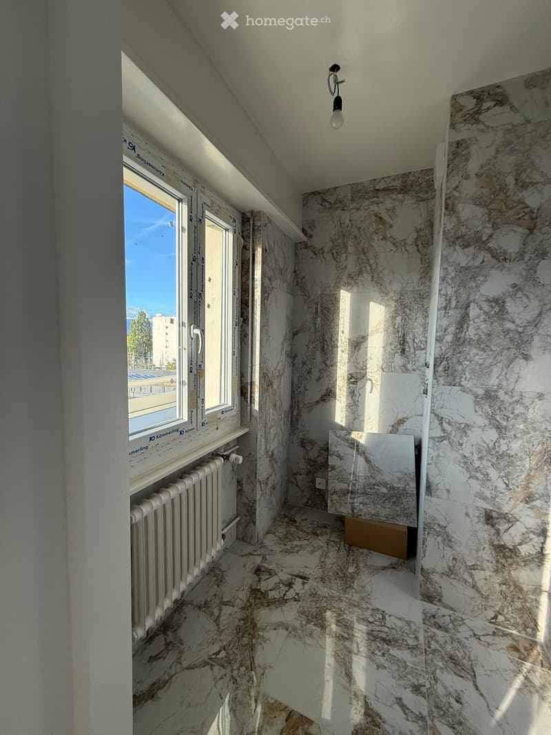 Narrow hallway with marble walls and floor, a radiator on the left, and a window at the end letting in natural light.