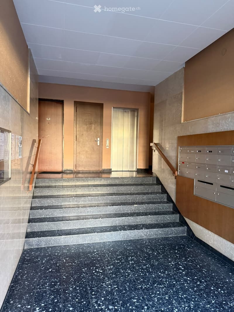 Staircase leading up with wooden handrails, marble steps, and mailboxes on the right side.