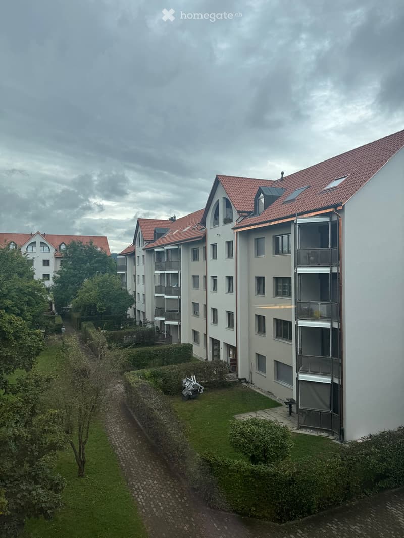 Modern multi-story residential building with red-tiled roofs, balconies, and surrounding greenery.