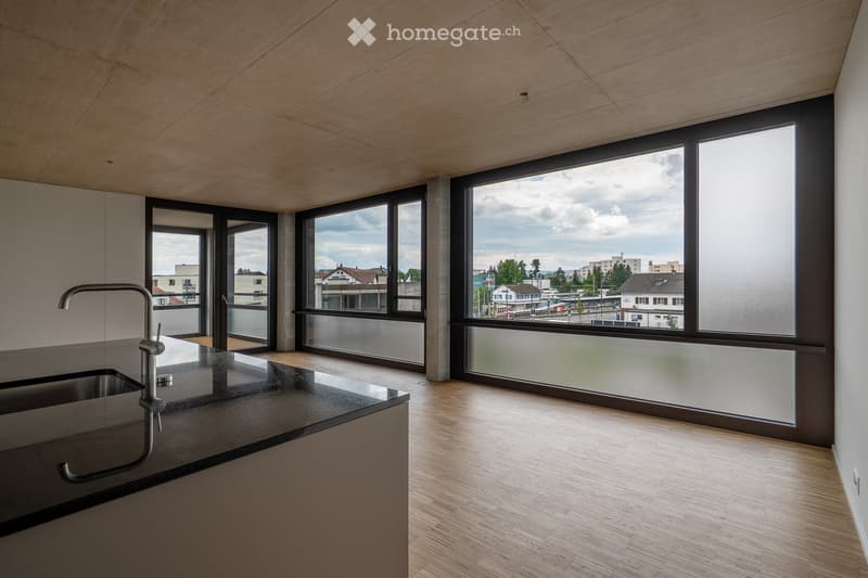 Modern kitchen with dark countertops, light wooden flooring, and large windows offering a view of the cityscape.