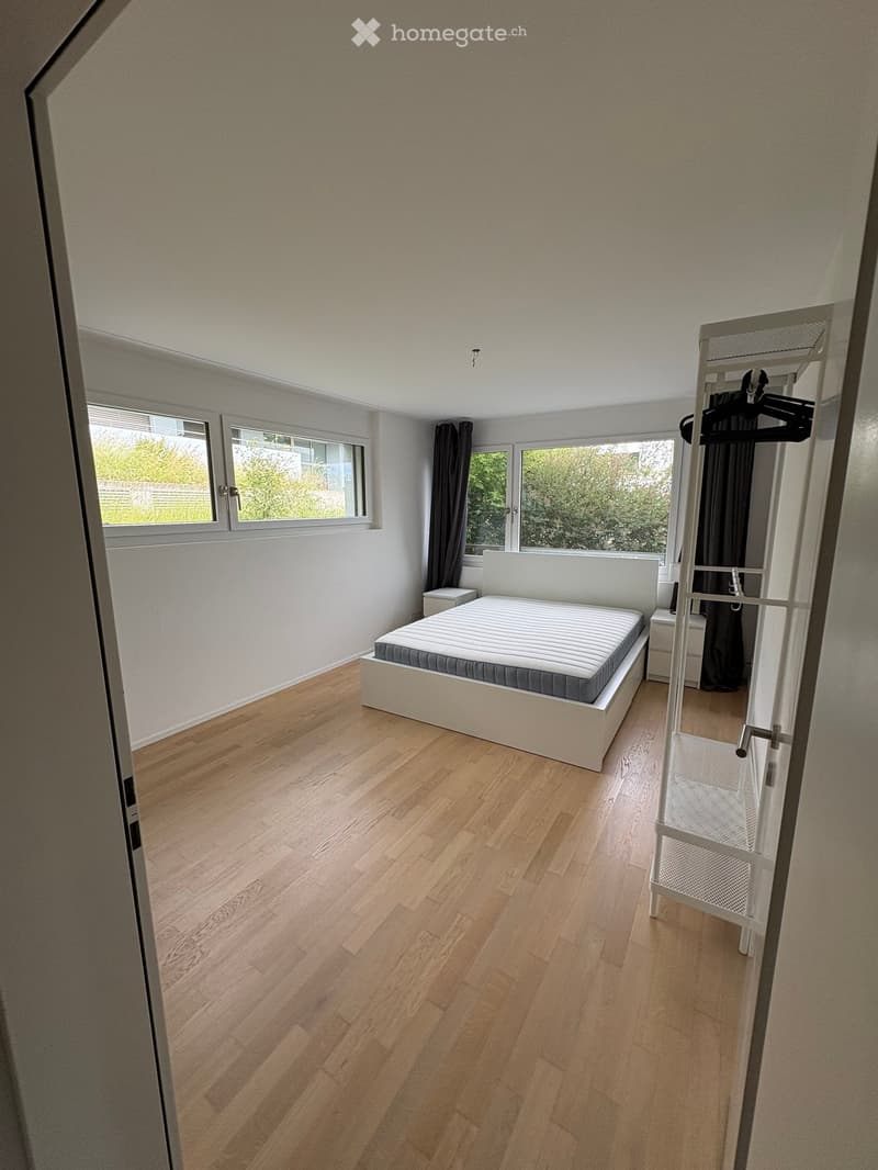 Modern bedroom with wooden flooring, white bed frame, nightstand, and built-in wardrobe with hanging space.