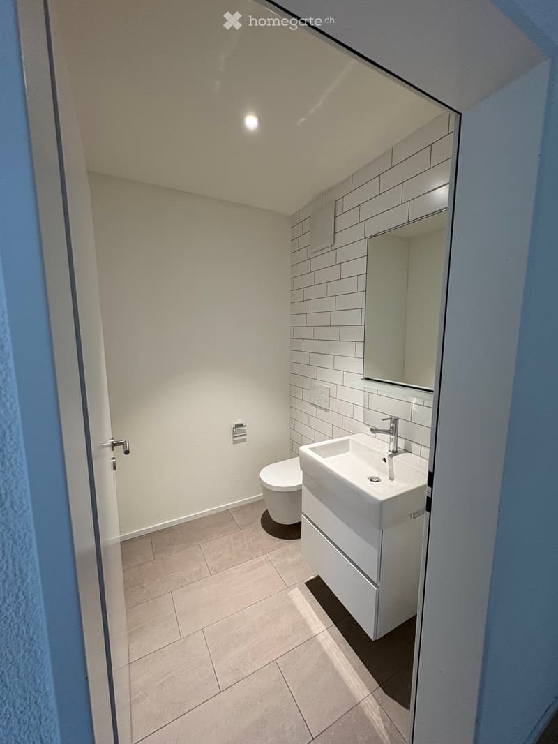 Modern bathroom with white tiles, a sink, toilet, and a mirrored cabinet.