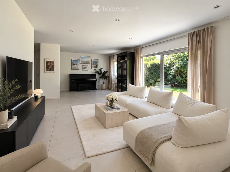 Modern living room with a white sectional sofa, coffee table, piano, bookshelf, and large windows overlooking a garden.