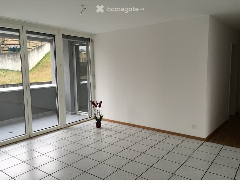 Empty room with tiled floor, white walls, large sliding glass doors leading to a balcony, and a small potted plant near the entrance.