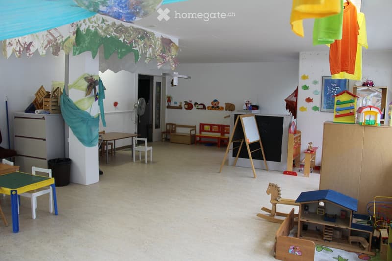 A brightly decorated children's play area with tables, chairs, toy houses, a rocking horse, and various colorful decorations.