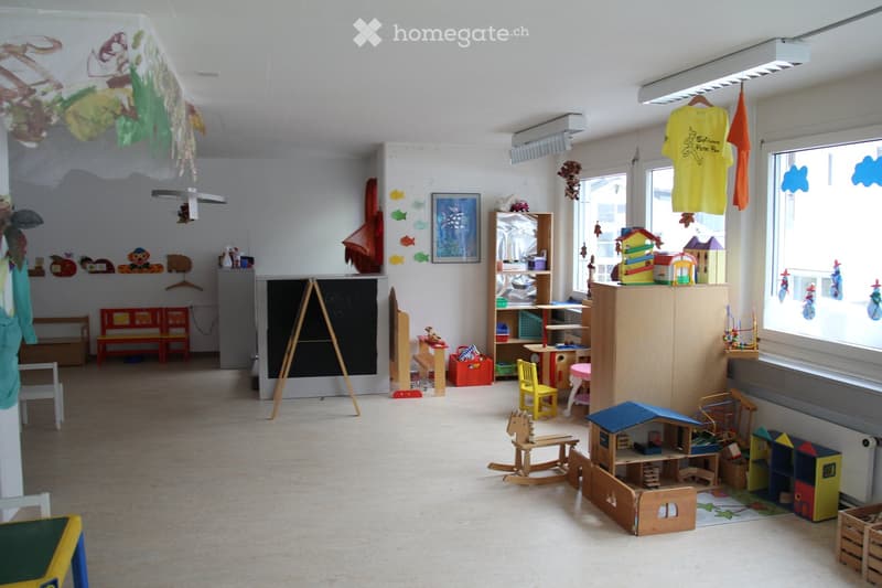 Brightly colored children's play area with benches, chairs, tables, shelves, toys, a rocking horse, and a dollhouse.