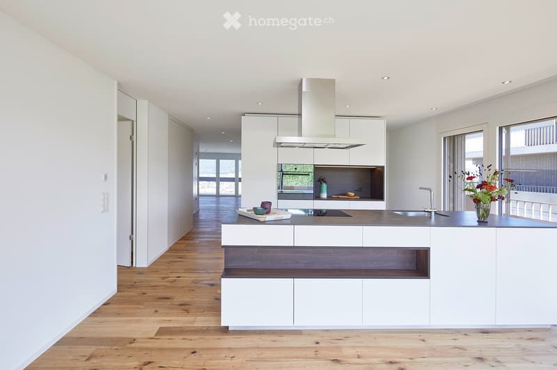 Modern kitchen with white cabinets, wooden flooring, central island, and built-in appliances.