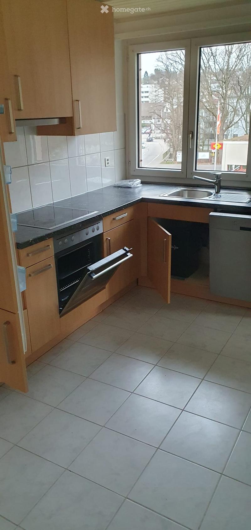 Modern kitchen with light wooden cabinets, tiled walls, and a black countertop. Features an oven, dishwasher, and sink.