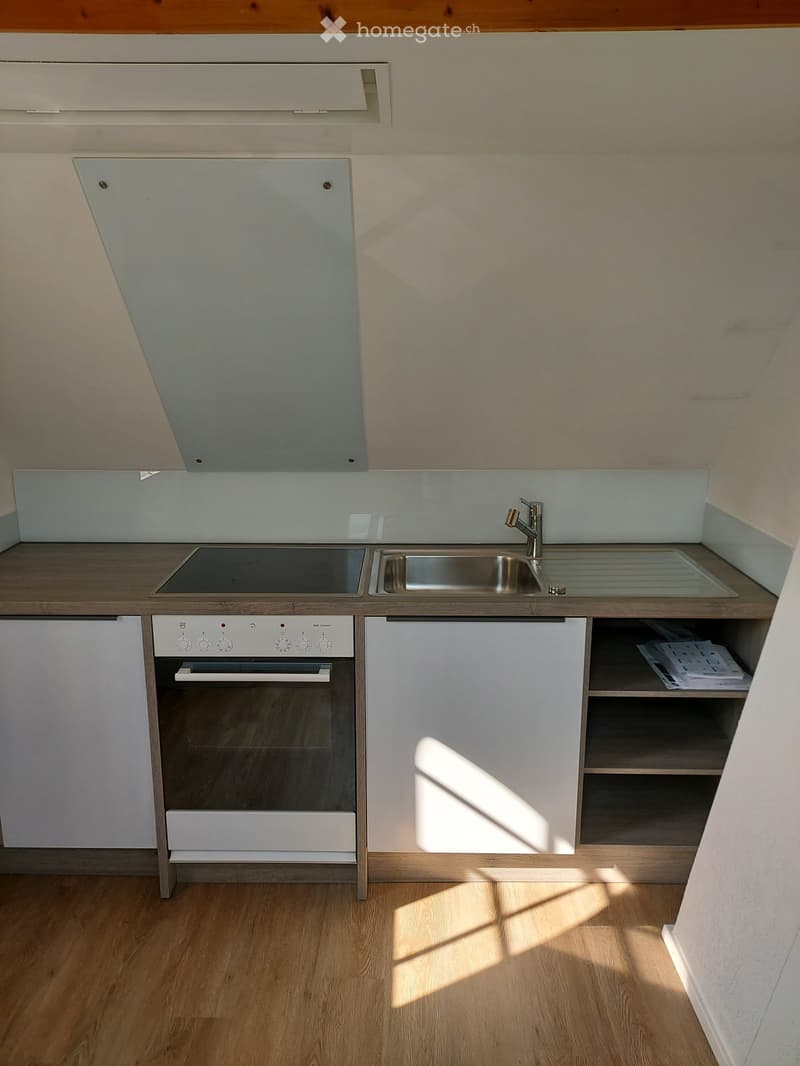 Modern kitchen with wooden flooring, white cabinets, stainless steel sink, and built-in oven.