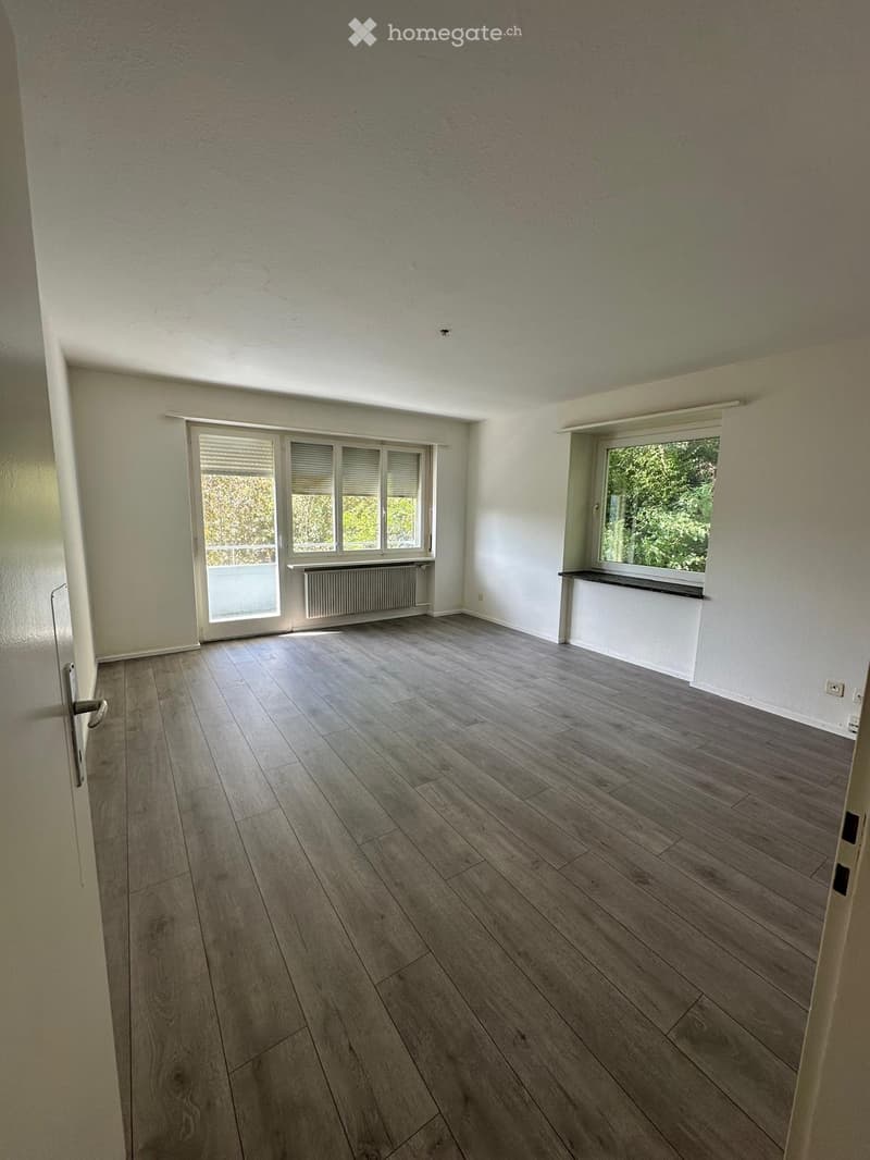 Empty room with wooden flooring, white walls, large windows, and a radiator. No furniture or equipment present.