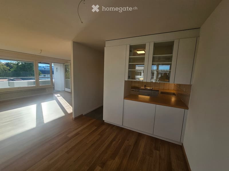 Modern kitchen with white cabinets, wooden countertop, and a sink. The space is bright with large windows and wooden flooring.