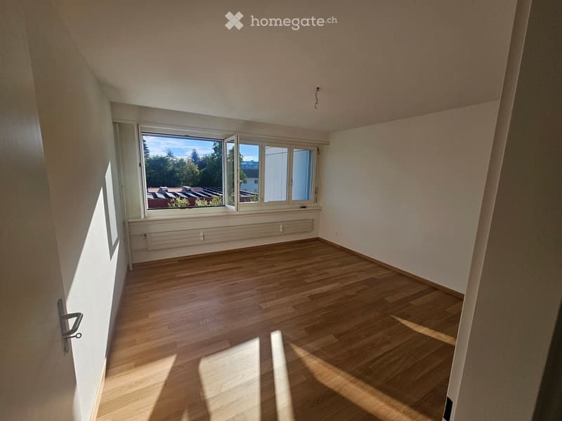 Empty room with wooden flooring, large windows, and white walls. No furniture or equipment present.