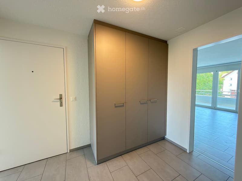 Empty hallway with tiled floor, white walls, and a large closet with double doors. A sliding glass door leads to a balcony or terrace area.