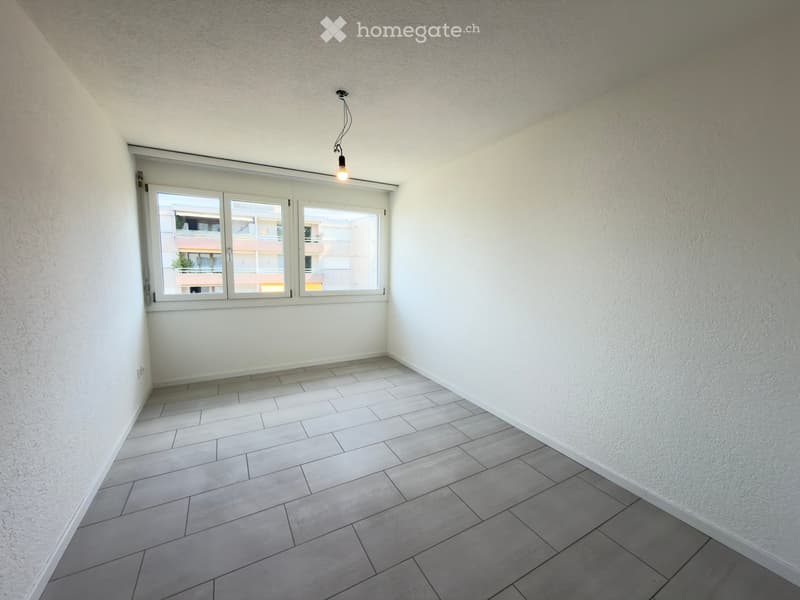 Empty room with tiled floor, white walls, and large windows with blinds. No furniture or equipment present.