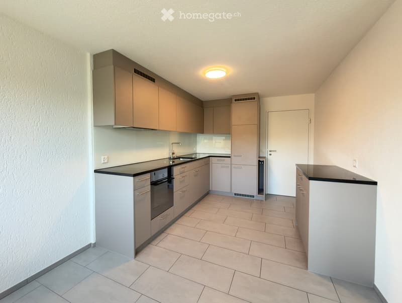 Modern kitchen with light-colored cabinets, a black countertop, and built-in appliances including an oven and refrigerator. The space features tiled flooring and a sleek, contemporary design.
