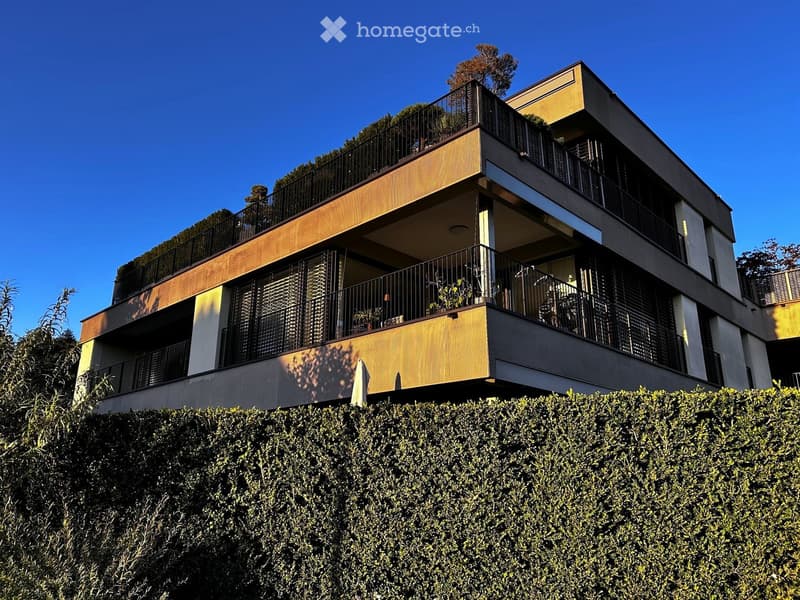 Modern multi-story building with balconies, wooden accents, and greenery on the roof.