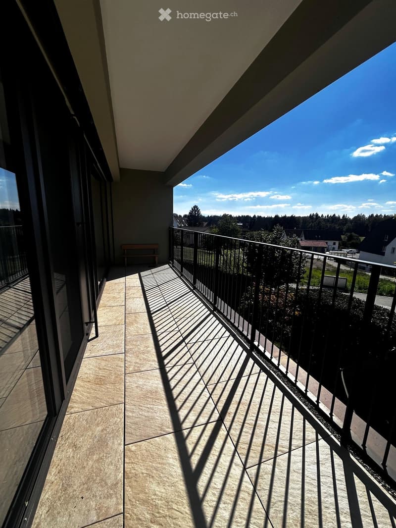 Balcony with tiled floor, metal railing, and a bench, overlooking a suburban area with trees and houses.