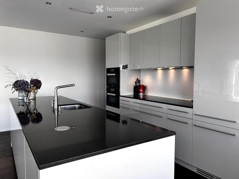 Modern kitchen with sleek white cabinets, black countertop, stainless steel sink and faucet, built-in oven, and decorative vases with flowers on the counter.